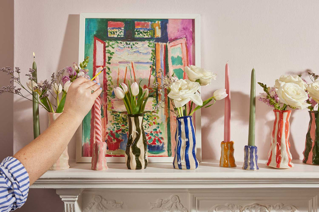 Colourful striped ceramic vases and candle holders with flowers displayed on a mantelpiece.