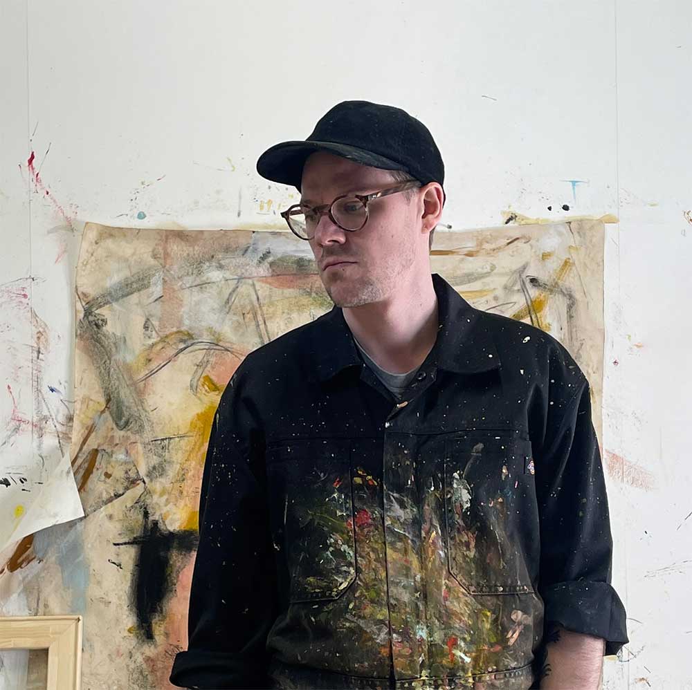 Sam Judge in his North Yorkshire studio, standing in front of one of his abstract paintings